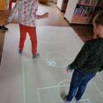 Uczniowie grają w wirtualną piłkę nożną wyświetlaną na podłodze